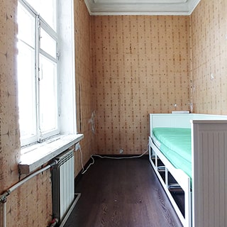 На фото: часть помещения жилой комнаты, в левой стене - одно окно с деревянными рамами, под окном - батарея центрального отопления, у правой стены - диван-кровать, стены оклеены обоями, пол - ламинат